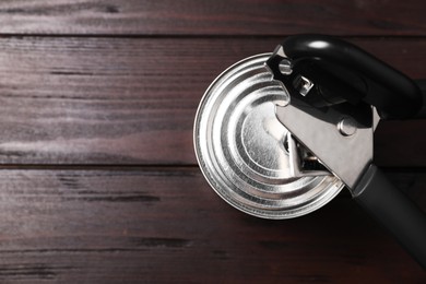 Photo of Can opener and tin on wooden table, top view. Space for text