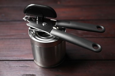 Photo of Can opener and tin on wooden table, closeup