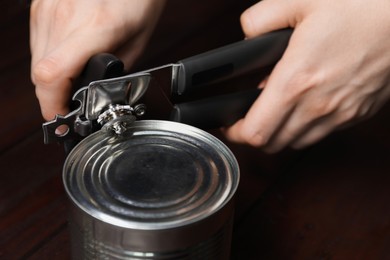 Photo of Woman opening tin with can opener at wooden table, closeup