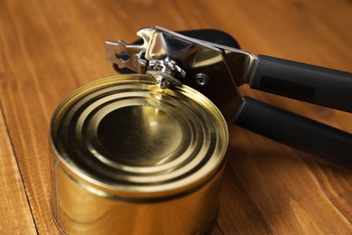 Photo of Can opener and tin on wooden table, closeup