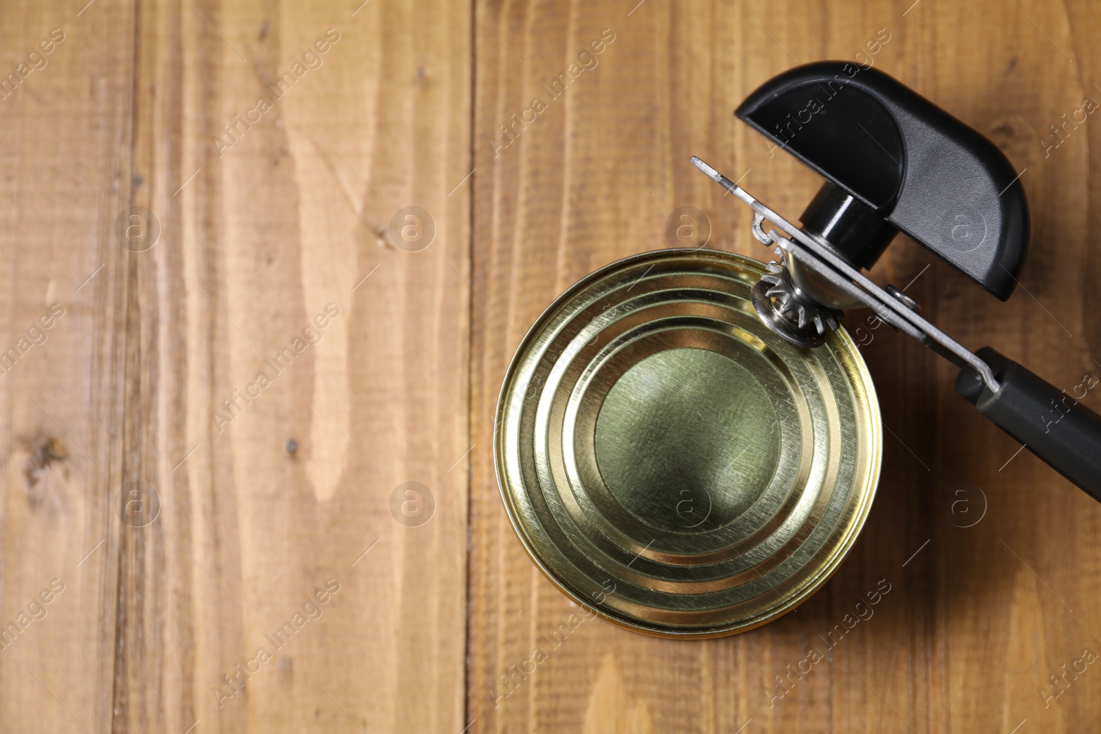 Can opener and tin on wooden table, top view. Space for text Photo of Can opener and tin on wooden table, top view. Space for text