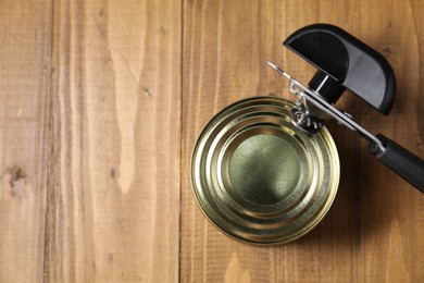 Photo of Can opener and tin on wooden table, top view. Space for text
