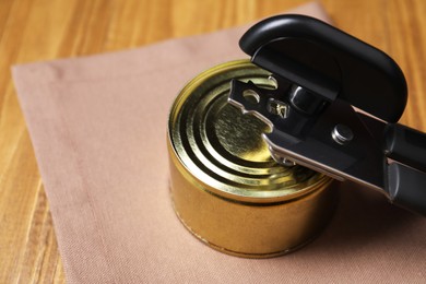Photo of Can opener and tin on wooden table, closeup. Space for text