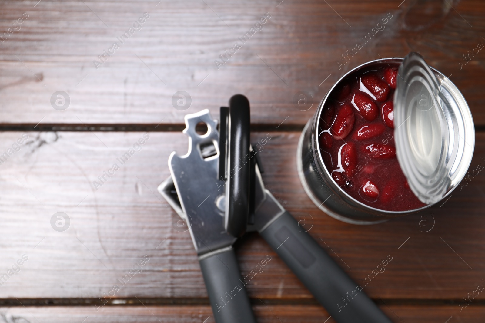 Can opener and tin with beans on wooden table, top view. Space for text Photo of Can opener and tin with beans on wooden table, top view. Space for text