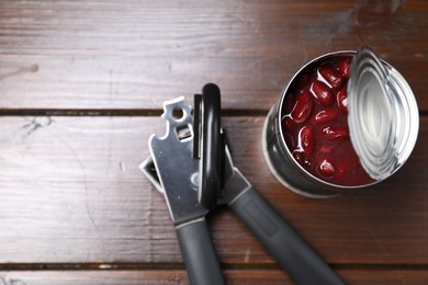 Photo of Can opener and tin with beans on wooden table, top view. Space for text