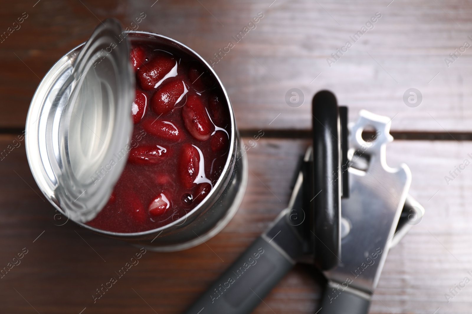 Can opener and tin with beans on wooden table, top view Photo of Can opener and tin with beans on wooden table, top view