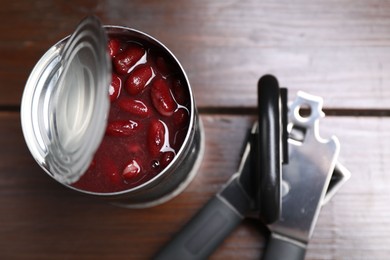 Photo of Can opener and tin with beans on wooden table, top view