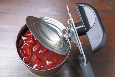Photo of Can opener and tin with beans on wooden table, top view