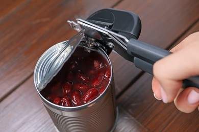 Photo of Woman opening tin with can opener at wooden table, closeup