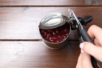 Photo of Woman opening tin with can opener at wooden table, closeup