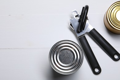 Photo of Can opener and tins on white wooden table, flat lay. Space for text