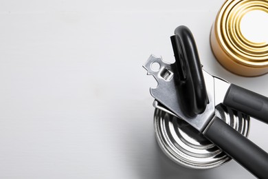 Photo of Can opener and tins on white table, flat lay. Space for text