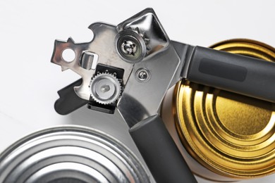 Photo of Can opener and tins on white table, flat lay