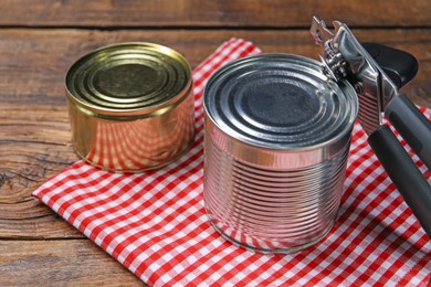 Photo of Can opener and tins on wooden table, closeup