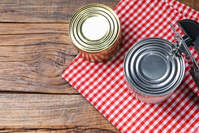 Photo of Can opener and tins on wooden table, flat lay. Space for text