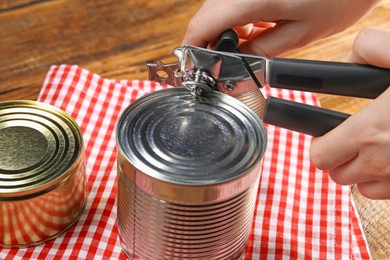 Photo of Woman opening tin with can opener at wooden table, closeup