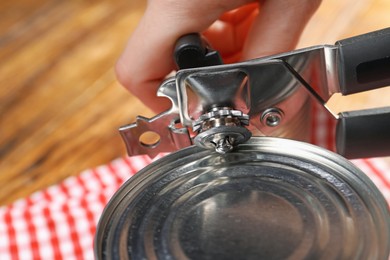 Photo of Woman opening tin with can opener at wooden table, closeup