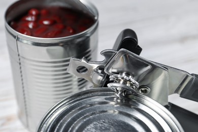 Photo of Can opener and tins on white table, closeup