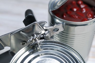 Photo of Can opener and tins on white table, closeup
