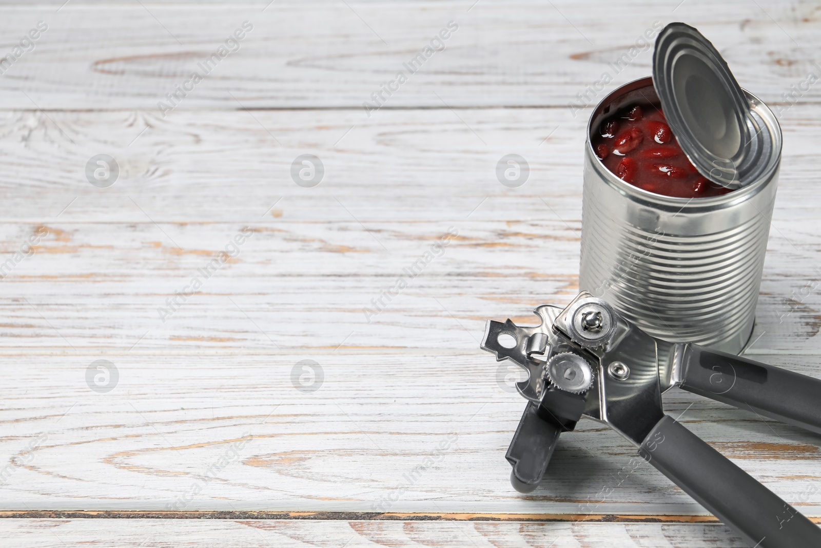 Can opener and tin with beans on white wooden table. Space for text Photo of Can opener and tin with beans on white wooden table. Space for text