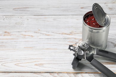 Photo of Can opener and tin with beans on white wooden table. Space for text