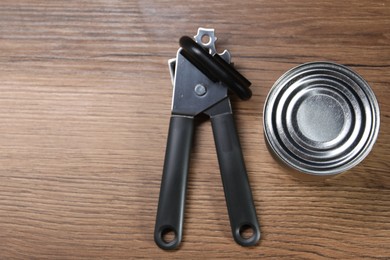 Photo of Can opener and tin on wooden table, top view. Space for text