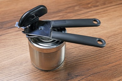 Photo of Can opener and tin on wooden table, closeup