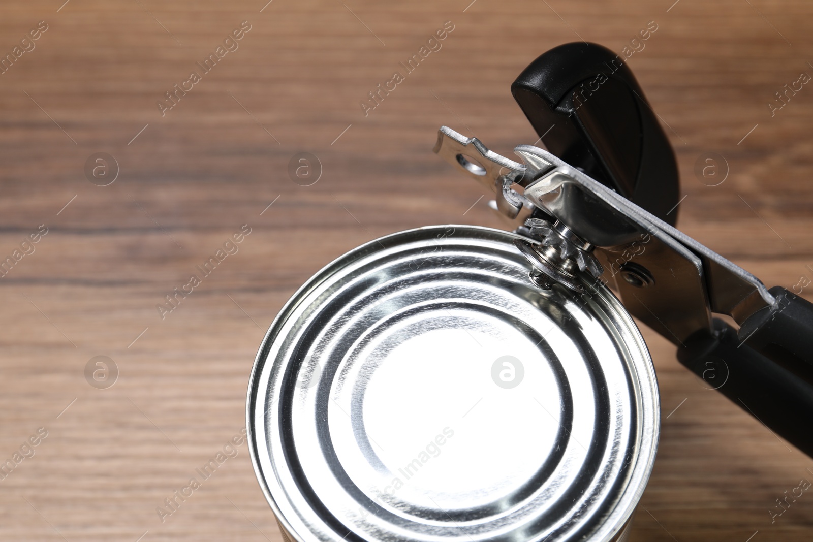 Can opener and tin on wooden table, closeup. Space for text Photo of Can opener and tin on wooden table, closeup. Space for text