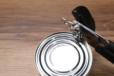 Photo of Can opener and tin on wooden table, closeup. Space for text