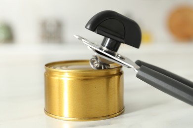 Photo of Can opener and tin on white marble table, closeup