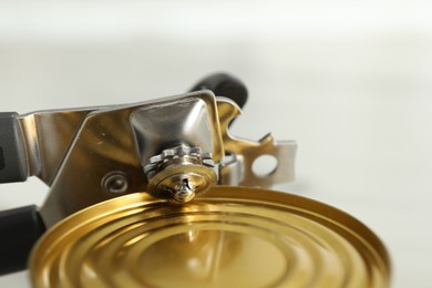Photo of Can opener and tin on blurred background, closeup