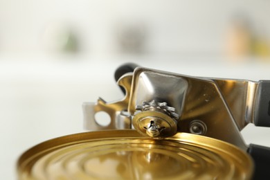 Photo of Can opener and tin on blurred background, closeup
