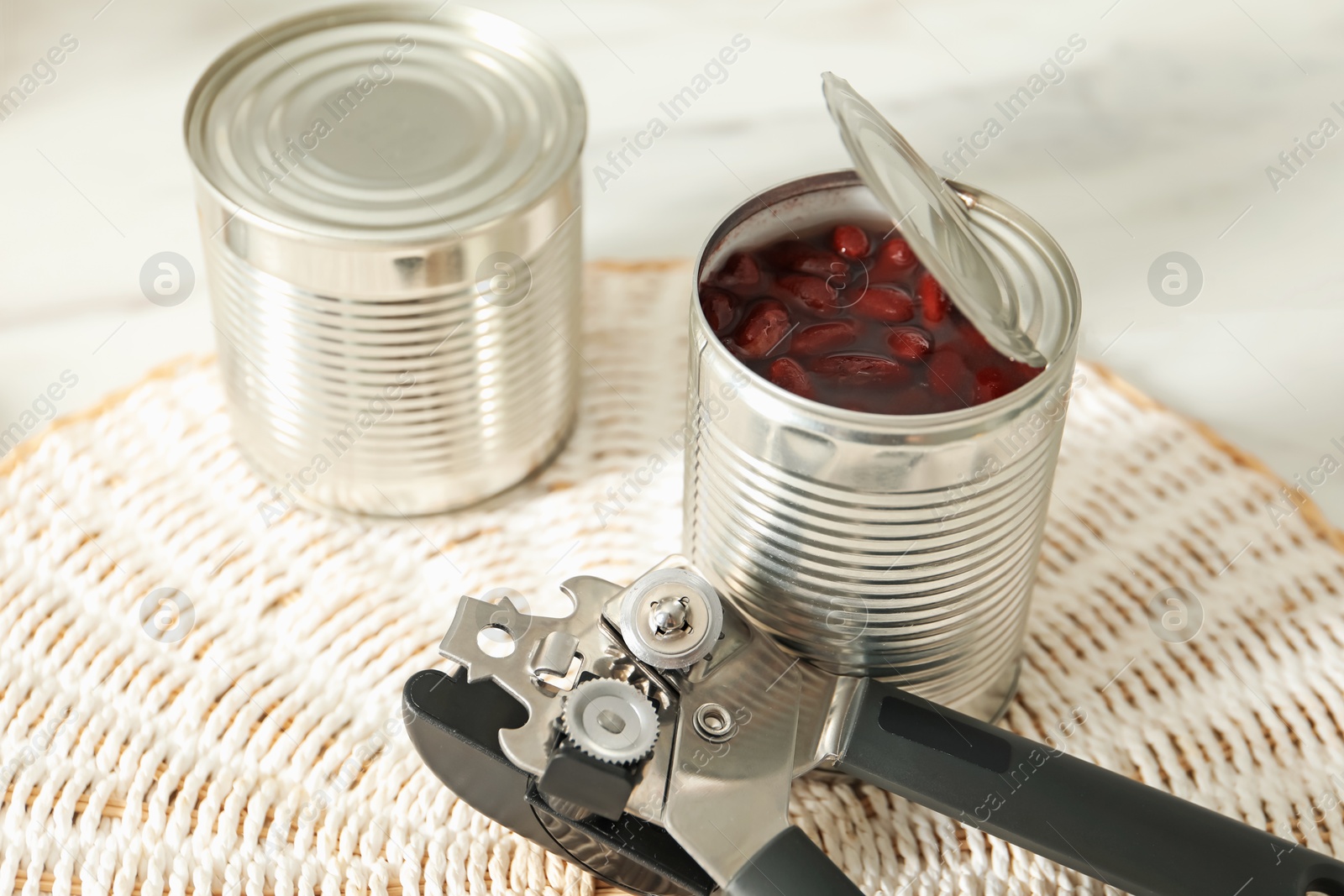 Can opener and tins with beans on white table, closeup Photo of Can opener and tins with beans on white table, closeup