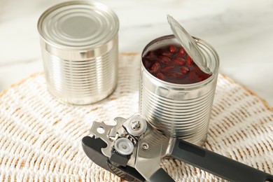 Photo of Can opener and tins with beans on white table, closeup
