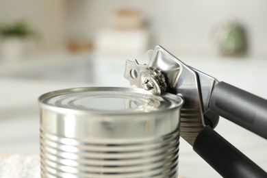 Photo of Can opener and tin on blurred background, closeup