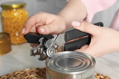 Photo of Woman opening tin with can opener at white table, closeup