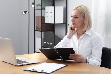 Photo of Professional psychologist with notebook and pen working with laptop at table in office