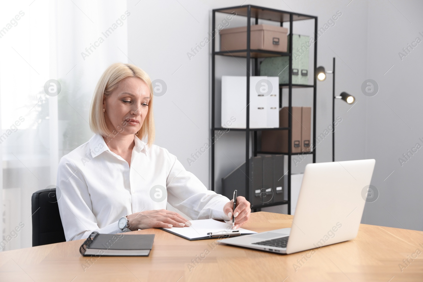 Professional psychologist taking notes while working with laptop at table in office Photo of Professional psychologist taking notes while working with laptop at table in office