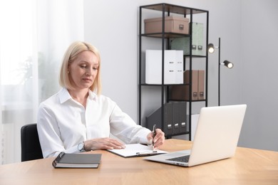Photo of Professional psychologist taking notes while working with laptop at table in office