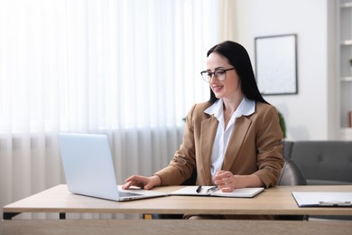 Photo of Professional psychologist taking notes while working with laptop at table in office