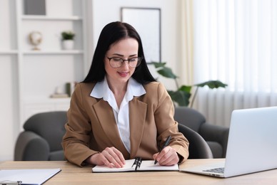 Photo of Professional psychologist taking notes while working with laptop at table in office