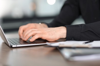 Photo of Man working on laptop at wooden desk in office, closeup