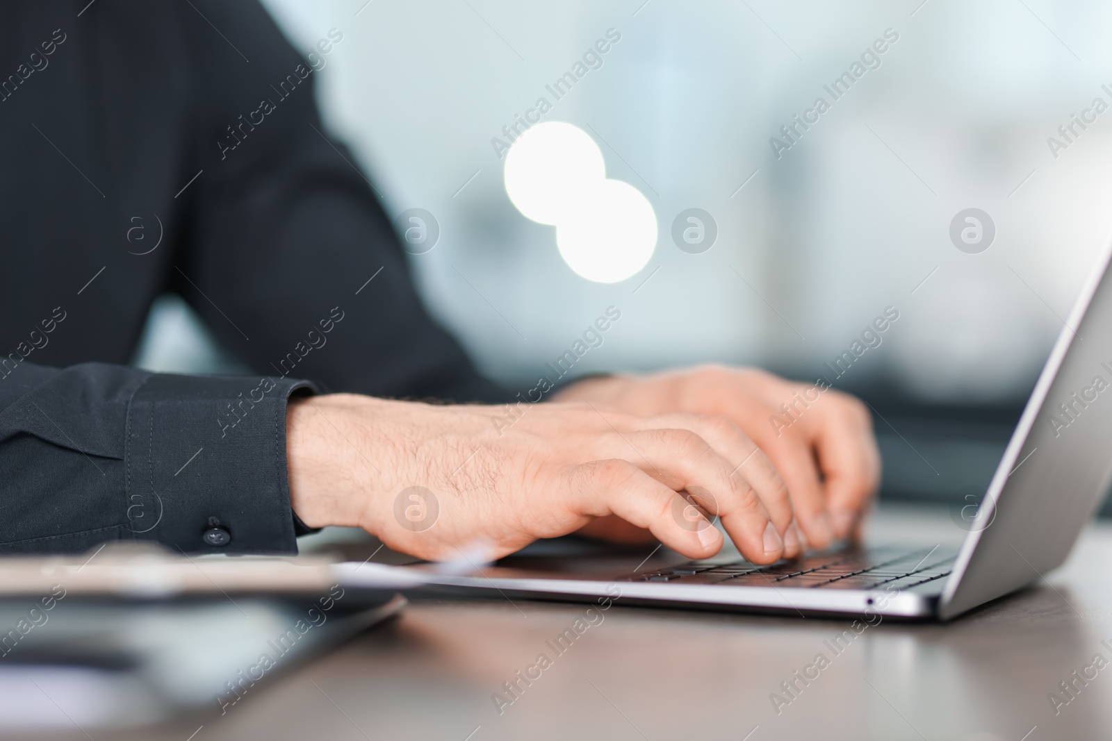 Man working on laptop at wooden desk in office, closeup Photo of Man working on laptop at wooden desk in office, closeup