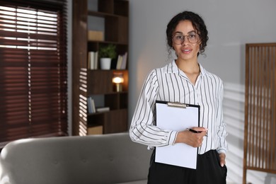 Photo of Professional psychologist with clipboard and pen in office, space for text