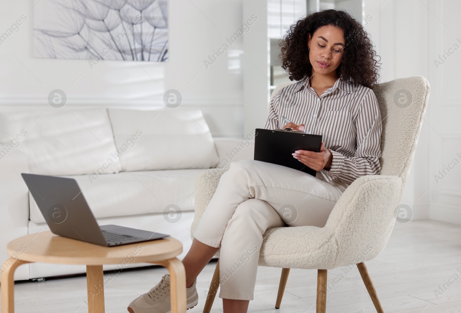 Professional psychologist taking notes while working with laptop in office Photo of Professional psychologist taking notes while working with laptop in office