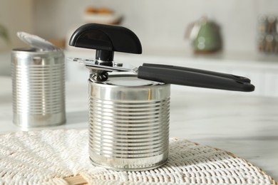 Photo of Can opener and tins on white table indoors, closeup