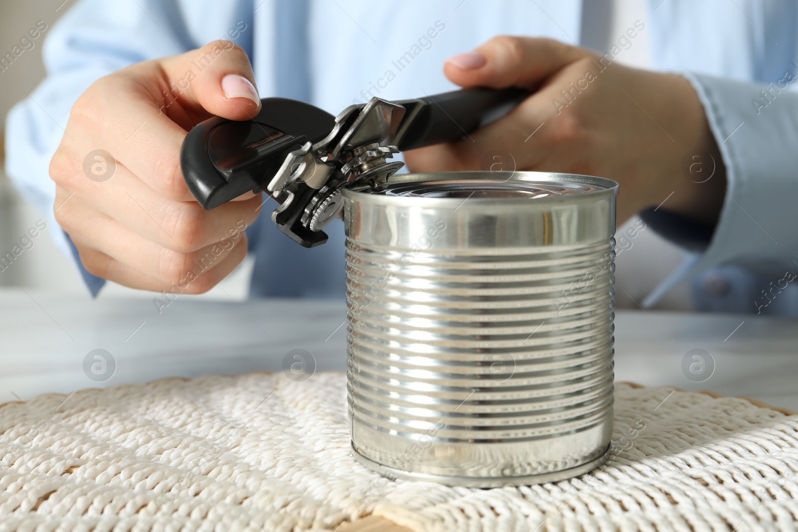 Woman opening tin with can opener at table, closeup Photo of Woman opening tin with can opener at table, closeup