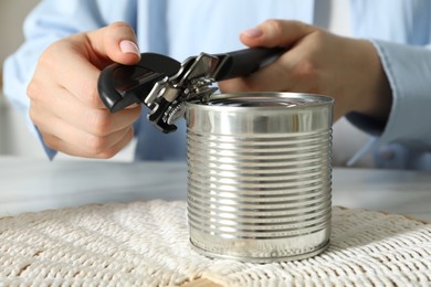 Photo of Woman opening tin with can opener at table, closeup