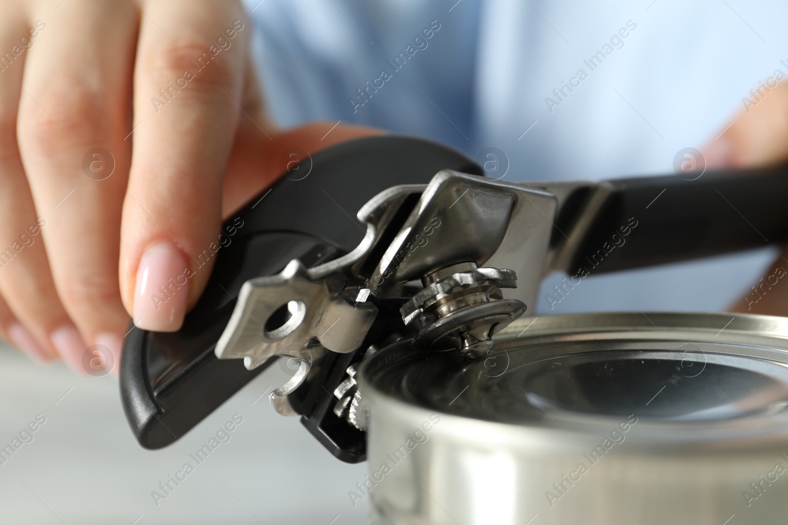 Woman opening tin with can opener at table, closeup Photo of Woman opening tin with can opener at table, closeup