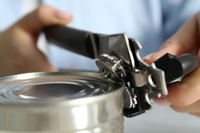 Photo of Woman opening tin with can opener at table, closeup